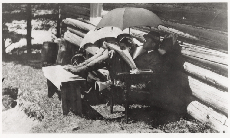 Charles Ives kicking back under an umbrella with a pipe and his wife. 