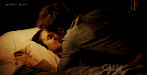 A couple from The Vampire Diaries kissing passionately on a bed