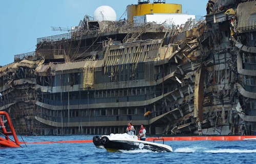 Salvage crew members pass by the damaged side of the Costa Concordia cruise ship as it emerges from water near Giglio, Italy.