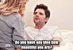 Ben in a hospital bed and gown, talking to Leslie