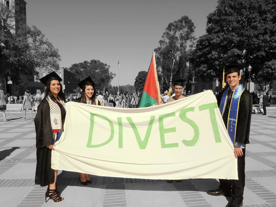 UCLA students stand around a Palestinian flag and a banner that reads "DIVEST".