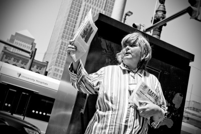 NEWSIE &#8212; A formerly homeless woman invites passers-by to purchase copies of the Cleveland Street Chronicle near Public Square in downtown Cleveland on May 23, 2012. Dolores Manley said she has been selling the street newspaper, which helps to support the homeless and formerly homeless, for more than 11 years. Licensed vendors like Manley purchase the paper for 35 cents and sell it for $1.25. The vendors keep the profit from each sale. Photo by Brandon Blackwell @CapturedCLE