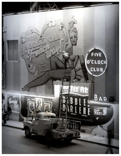 In a press photo dated from the mid-1950′s, a worker can be seen making repairs to the signage at Martha Raye’s Original &lsquo;5 O’CLOCK CLUB’ ; located at 215 22nd Street (at Collins Avenue), in Miami Beach.. Burlesque dancers Tee Tee Red and