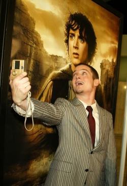 Famous face (Elijah Wood takes his own photo in front of a Lord of the Rings poster)