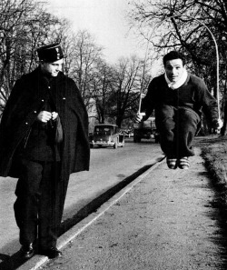 Un gendarme curieux regarde le champion des poids coqs Robert Cohen sauter à la corde à Paris, Bois de Boulogne, 1955. A curious gendarme stares as bantamweight champion Robert Cohen skips rope in Paris, Bois de Boulogne, 1955.