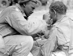 severinar:  An American soldier helps a comrade remove metal shrapnel from his face during the Invasion of Normandy, two days after the initial Normandy landings. France. 8 June 1944. 