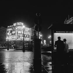 undr: Harry Kerr. Tourists read a map at Piccadilly Circus, near the statue of Eros. 1956