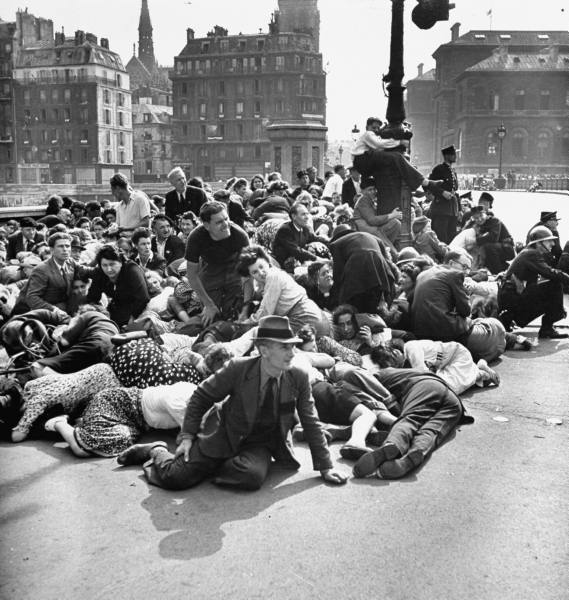 Crowd of frightened Parisians duck down to evade German sniper fire following the Nazi surrender of Paris, 1945.