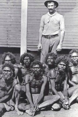 historicaltimes:  Australian man stands with his captive and chained Aboriginals Early 1900s 