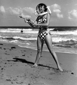 Bunny Yeager pointing a ray gun, wears a space helmet with her bikini on Miami Beach, Florida, 1952.