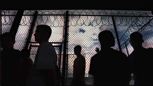 Young men silhouetted against a prison fence