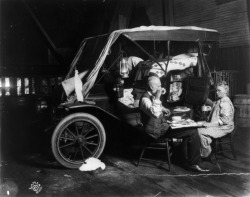An elderly couple enjoy a meal outside of their automobile home, 1911.