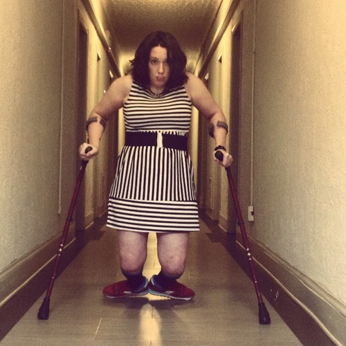 This photo was taken in the hallway of Natalie's apartment building. Natalie falls down several times a week. Sometimes, she is able to get up using her upper body strength and the crutches; sometimes, she needs help, In this photo, she is alone, staring straight at the camera. She is in the middle of getting up from a fall. She’s wearing a black-and-white “mod” style striped dress, a black and silver belt, and red sneakers. Her feet are almost in “second position,” heals touching and unable to point forward. Her knees are bare, and about one foot above the beige tile. Neither Natalie nor Denise know whether she will be able to push herself fully into a standing position. (About 10 seconds later, she does.) Natalie was most worried about this photo because she only has enough arm strength for two or three standing attempts before her body is too weak to get up without assistance.