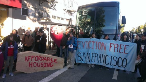 Photo of protesters in front of a bus holding a banner that reads 