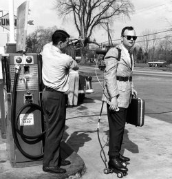 A salesman having his motorized roller skates refueled at a gas station (1961)