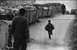 fotojournalismus:  Sarajevo, 1993. In the frontline district of Dobrinja, garbage containers and sandbags protect passers-by from Serbian sniper fire. A young boy runs along, his small height making it unnecessary for him to duck down like adults when